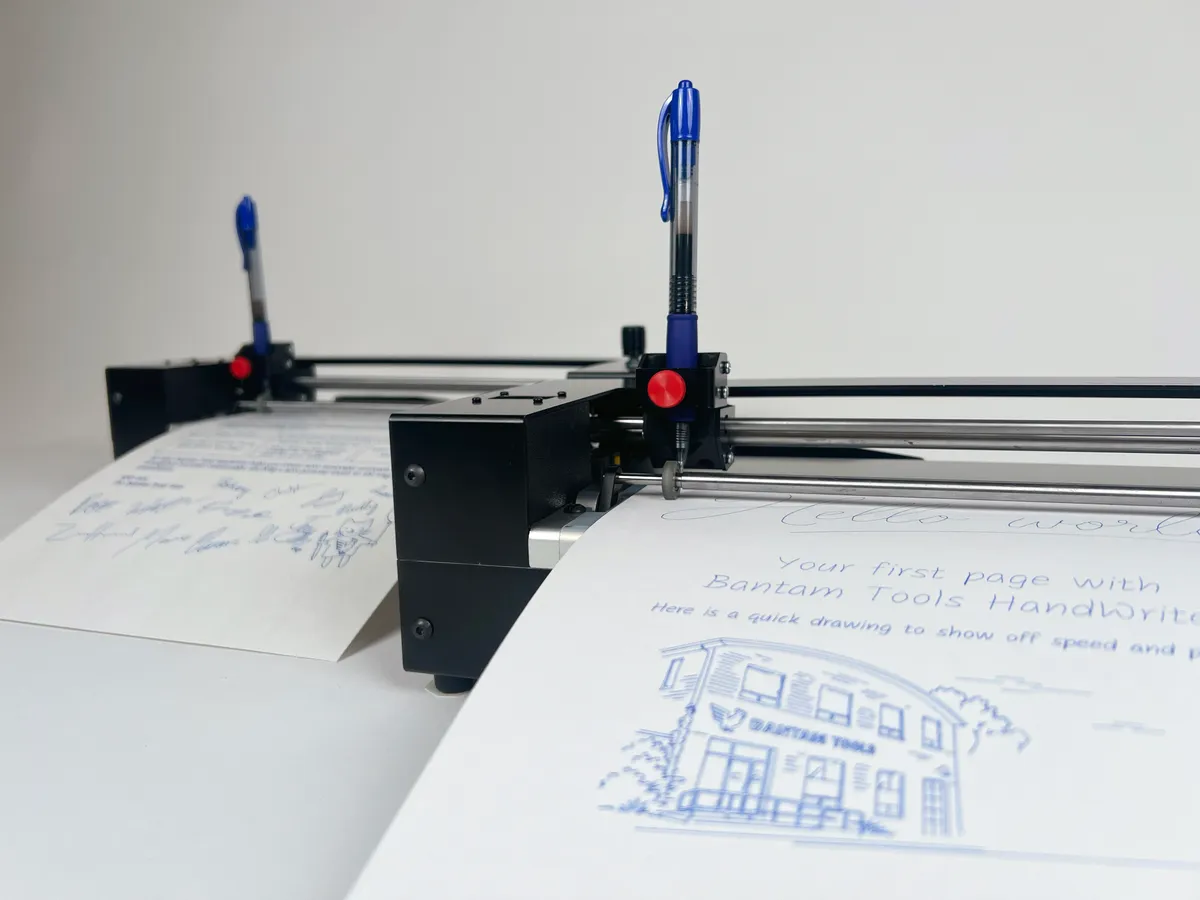Two Bantam Tools HandWriter® machines fitted with blue pens, with handwritten sample pages